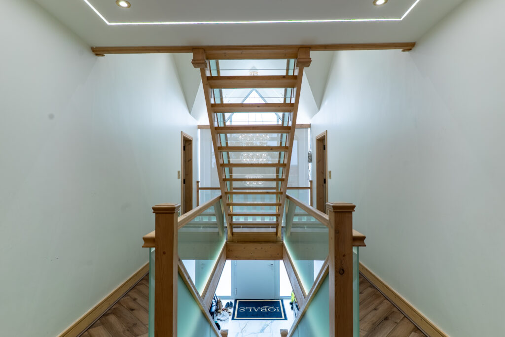 Open timber staircase with glass balustrades viewed from an upper landing